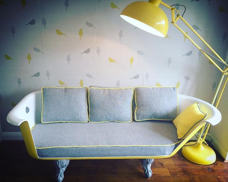 Old bathtub into yellow sofa with cushioned seats 