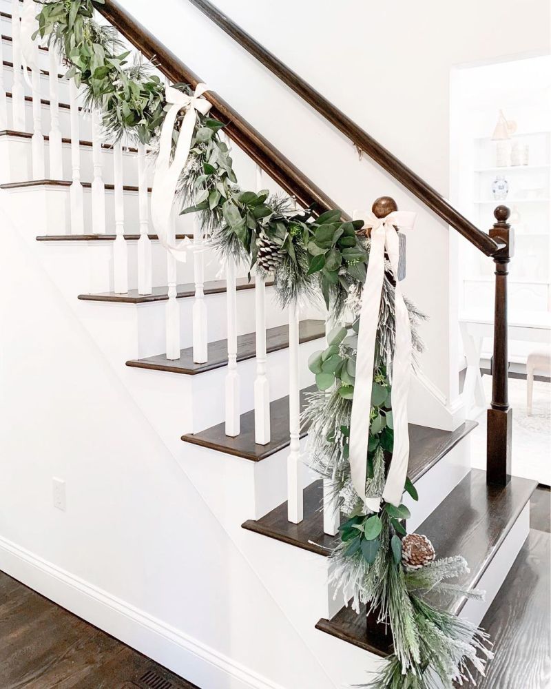 Green leaves garland, pin cones and white ribbon for staircase decor 