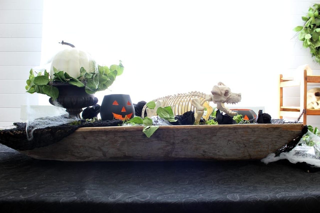 Doughbowl centerpiece with black pumpkin lanterns, leaves, skeleton dog, and black faux roses