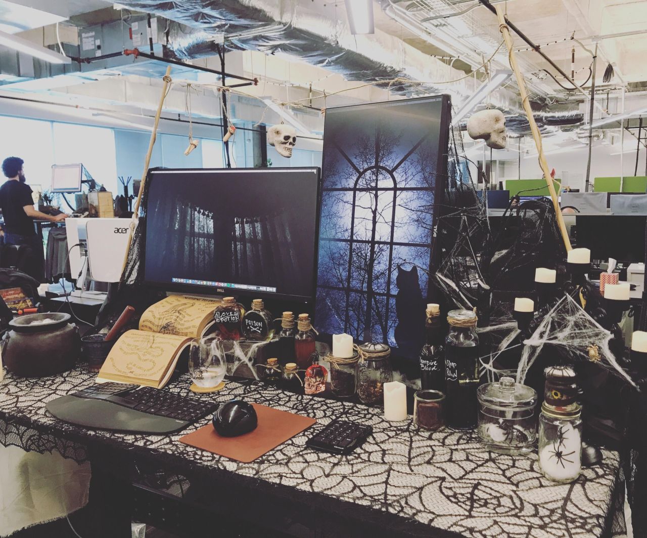 Office desk becomes a witch’s corner for Halloween with poison bottles, caldron and a creepy cat wallpaper