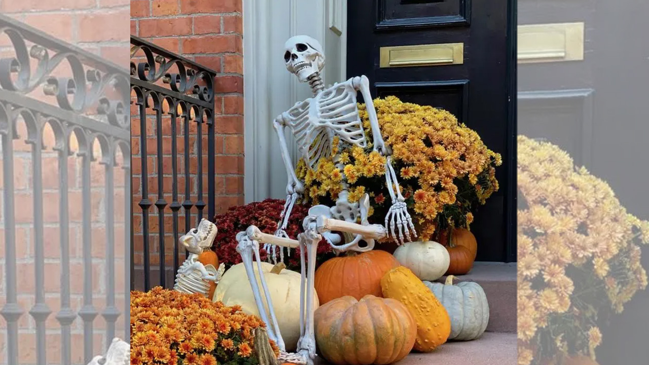 Porch steps are decorated with potted flowers, fresh pumpkins and skeletons for Halloween