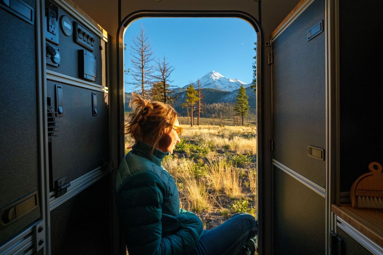 Four Wheel Campers CampOut Slide-In Truck Camper with Modular Interior Design - woman sitting on a door